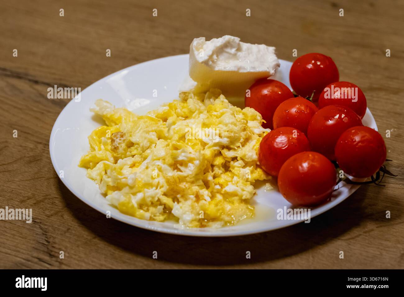 scrambled eggs with fresh cherry tomatoes on white plate Stock Photo