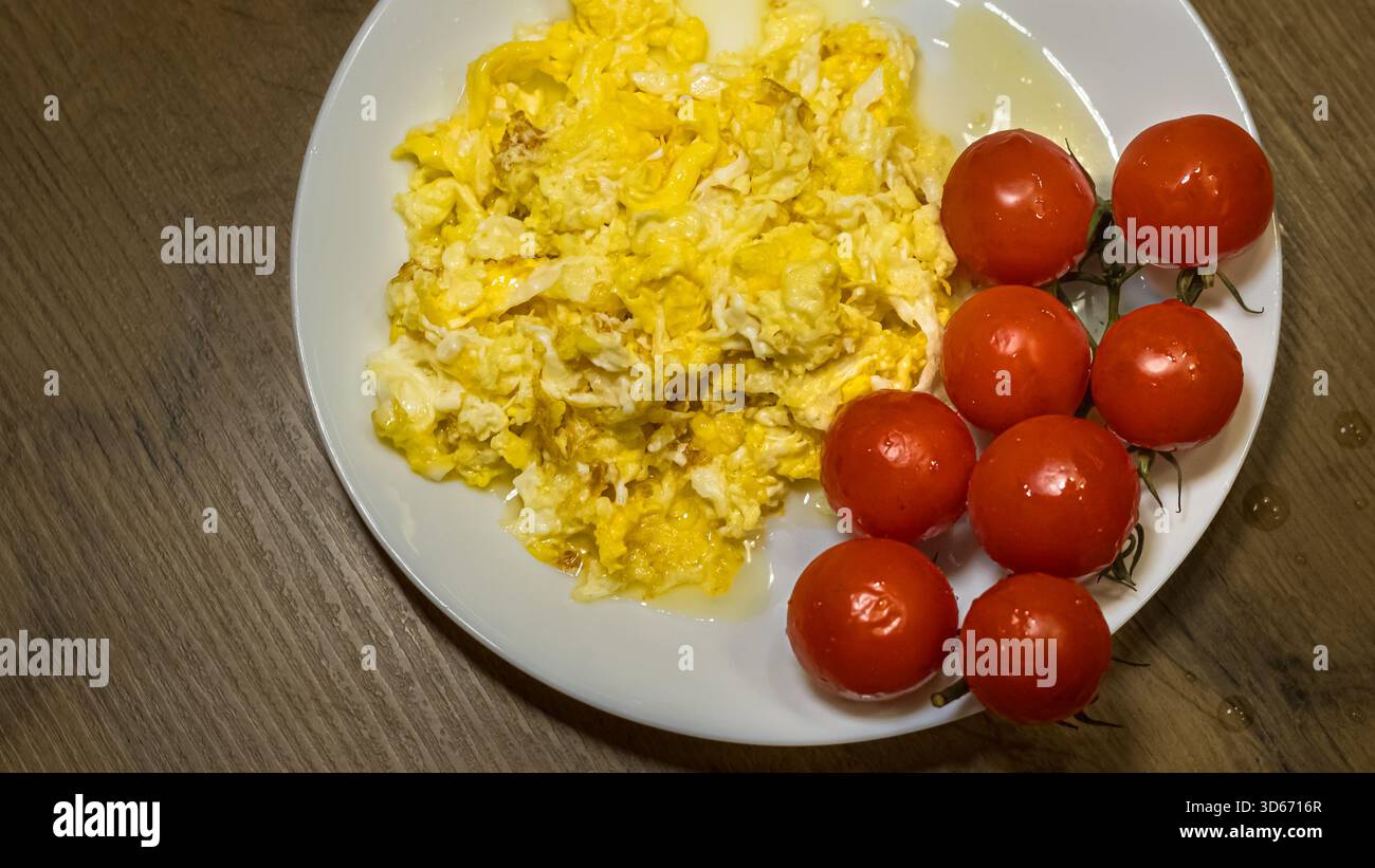 scrambled eggs with fresh cherry tomatoes on white plate_ Stock Photo