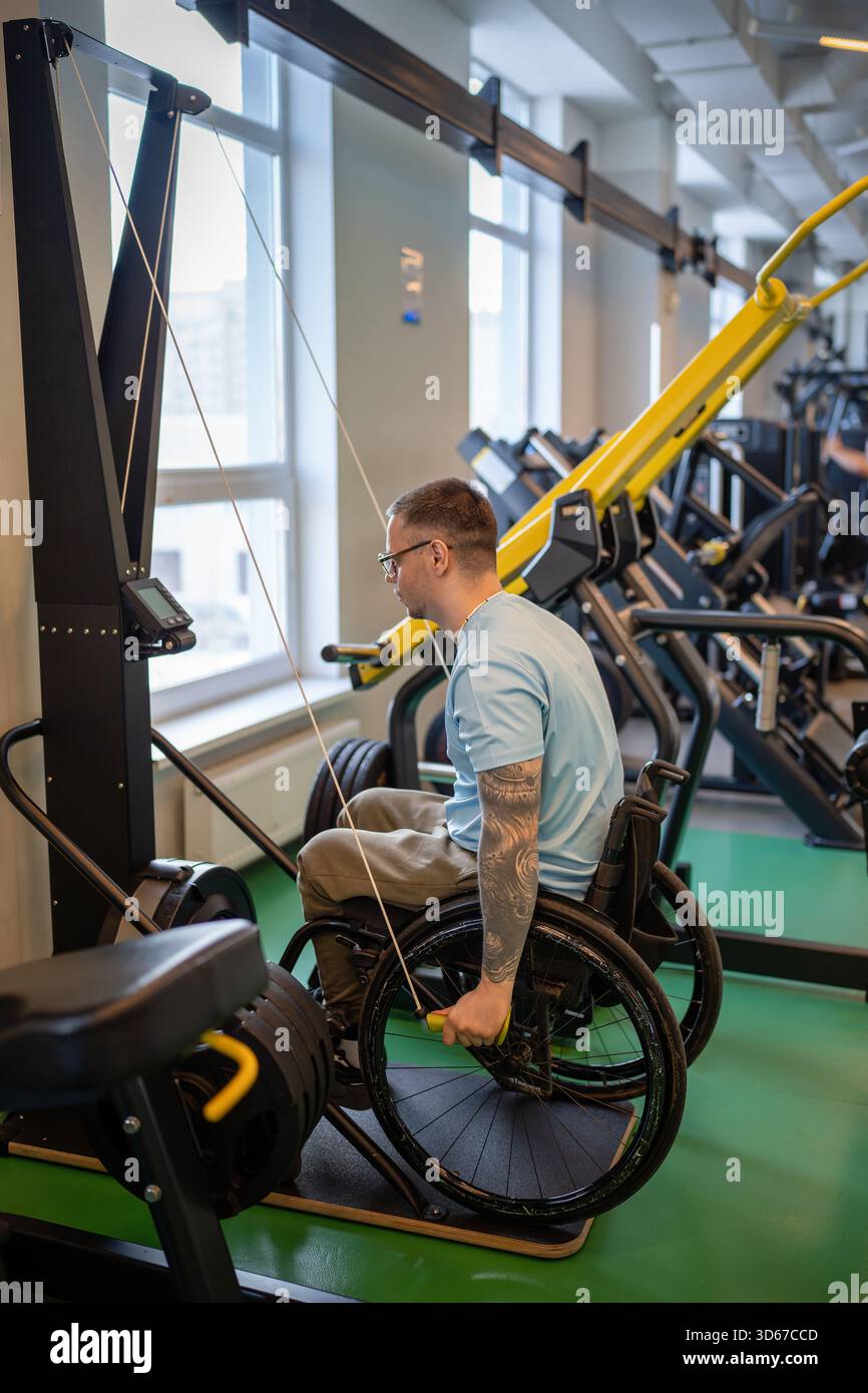 Disabled man in wheelchair doing vertical pulls with arms, workout for post injury rehabilitation. Stock Photo