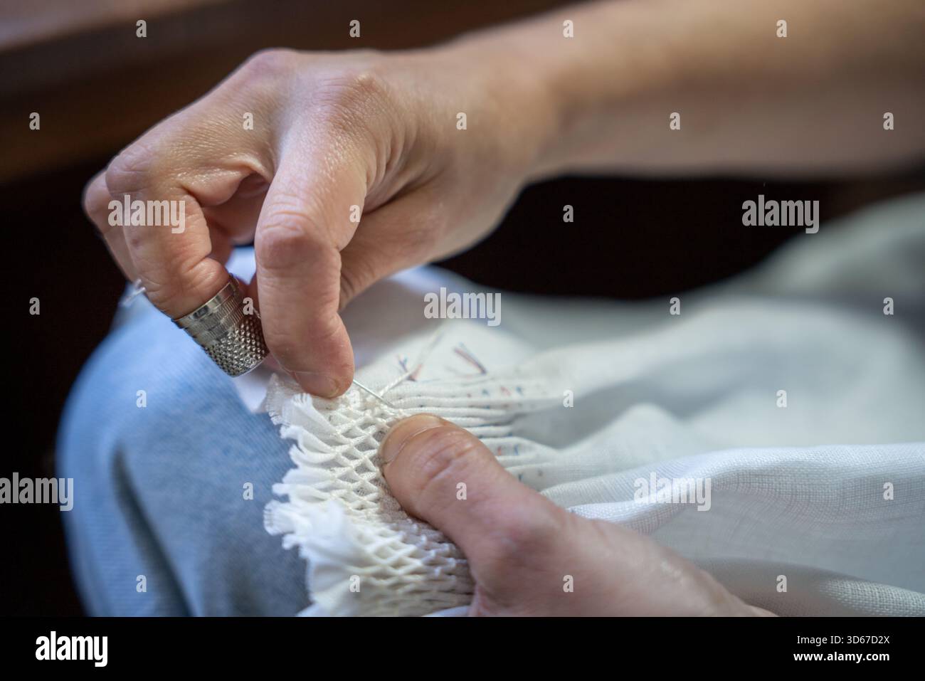 Hands creating smocking stitches on white fabric using a needle, thread, and thimble Stock Photo