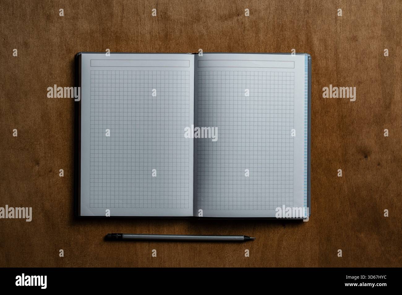 Open notebook with checkered sheets and pencil on wooden texture background, close up, top view, copy space Stock Photo