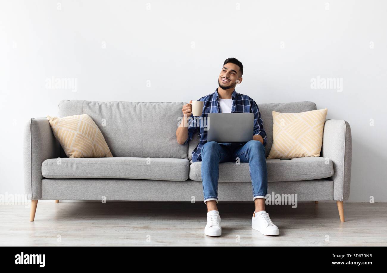 Man using pc sitting on the couch, drinking coffee Stock Photo