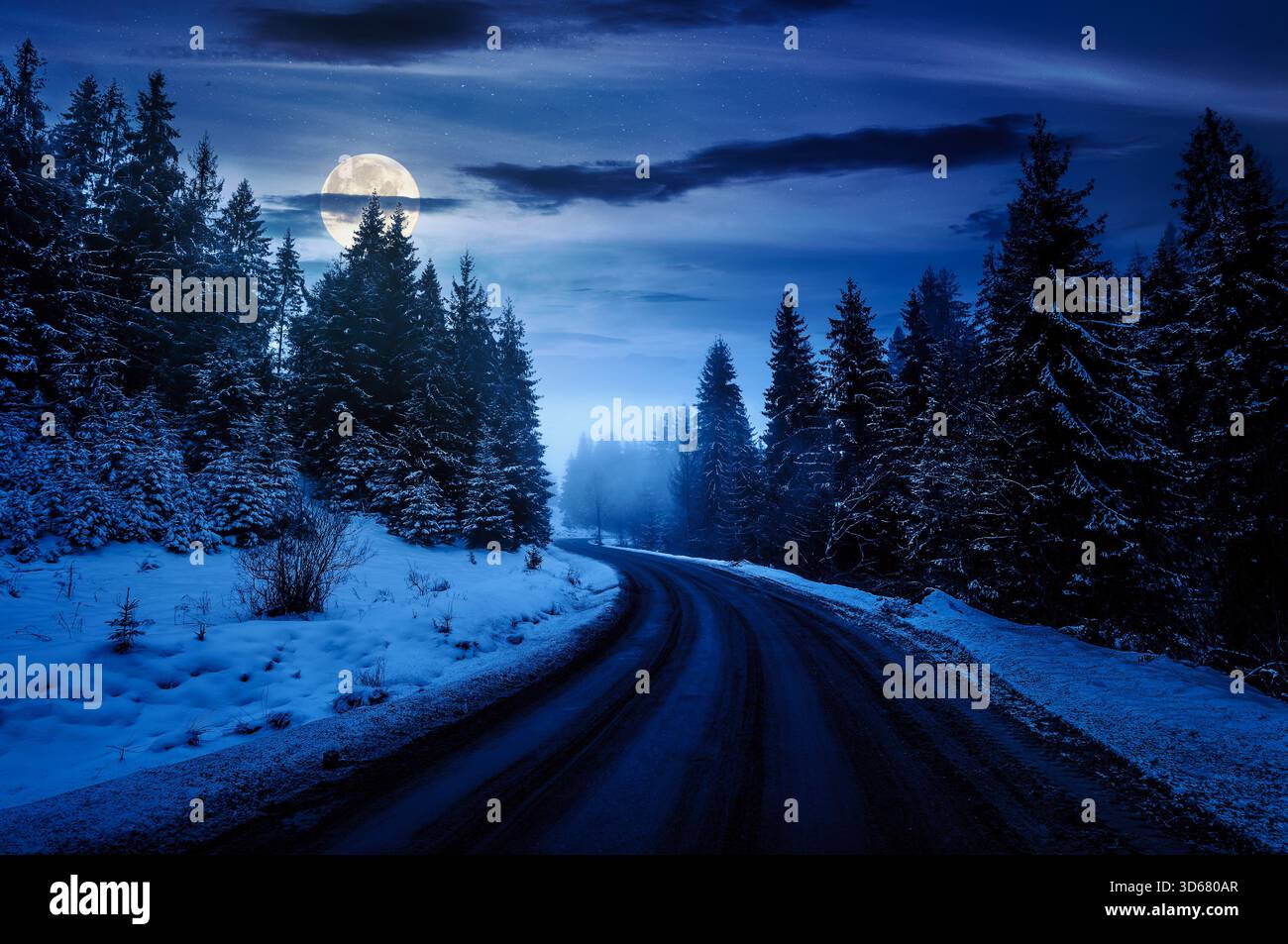 country road winding through spruce forest in winter at night. spooky nature landscape on foggy weather in full moon light. transportation background. Stock Photo