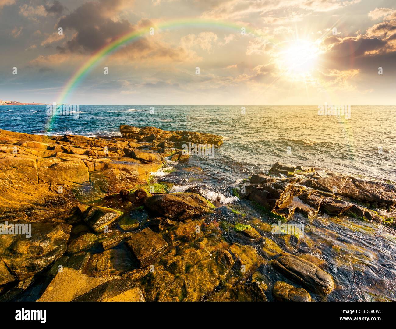 sunset at the rocky sea beach. beautiful view of coast landscape in summer. sun over horizon and cloudy sky. dramatic scenery with rock formations und Stock Photo