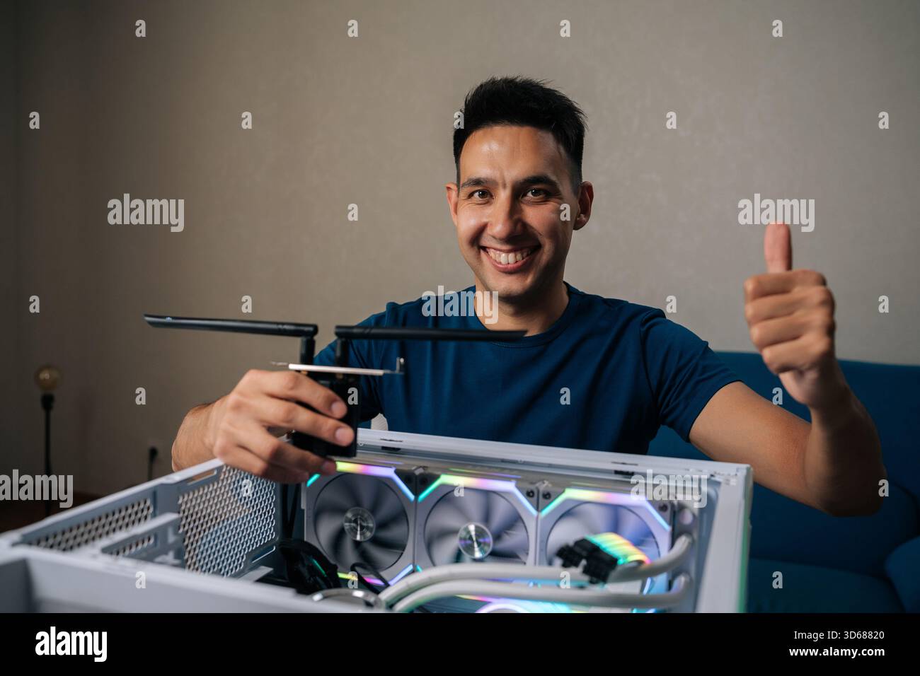 Cheerful computer technician smiling looking camera during installing wi-fi module into custom-built desktop computer with RGB lighting, showing Stock Photo