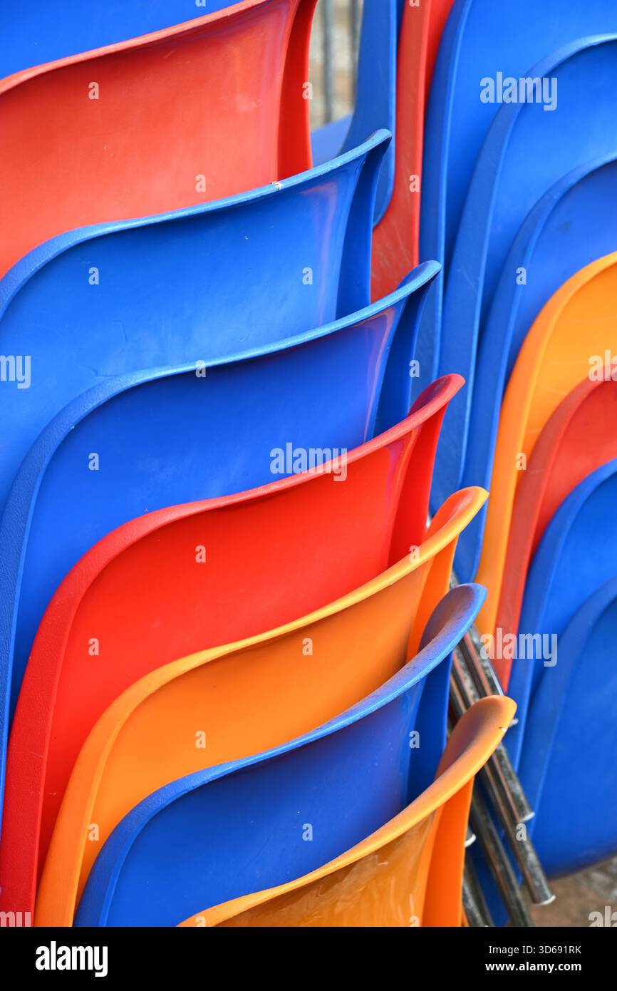 Colourful or Colorful Curvilinear Patterns or Abstract Patterns of Stacked Red, Orange & Blue Molded Plastic Chairs or Plastic Furniture Stock Photo