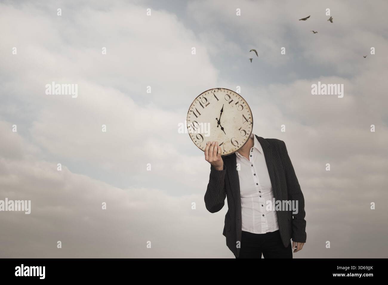 Person with clock in front of face under a cloudy sky, concept of time and business Stock Photo