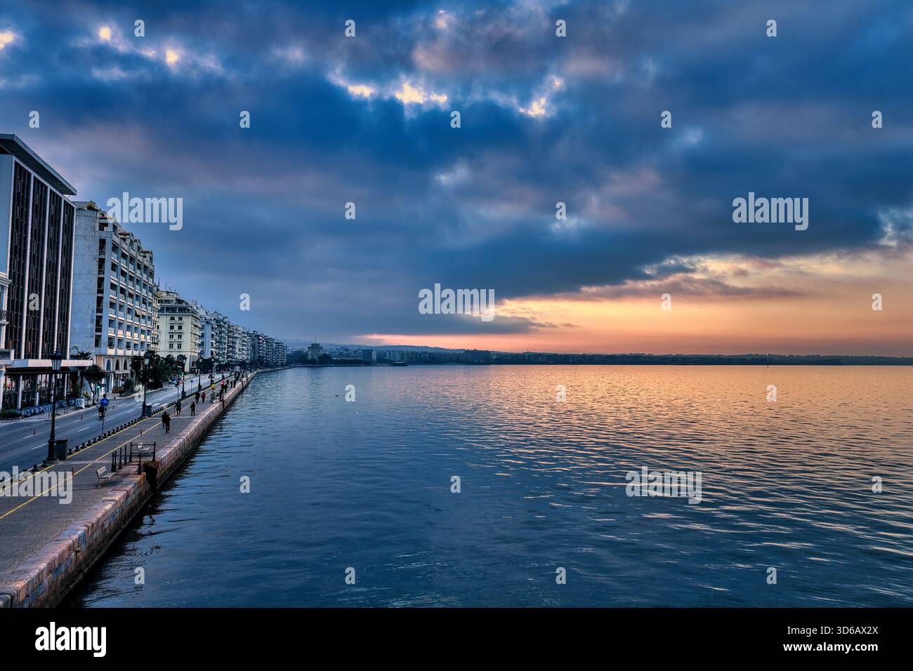 Dark clouds loom over Thessaloniki’s waterfront as morning light breaks through. The White Tower stands firm, watching a city awaken beneath a shiftin Stock Photo