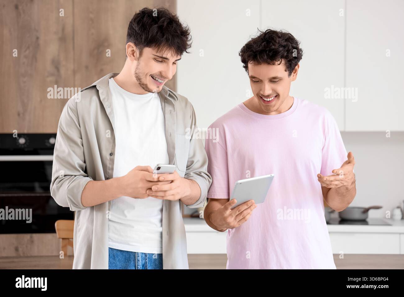 Young brothers using tablet computer and mobile phone in kitchen Stock Photo