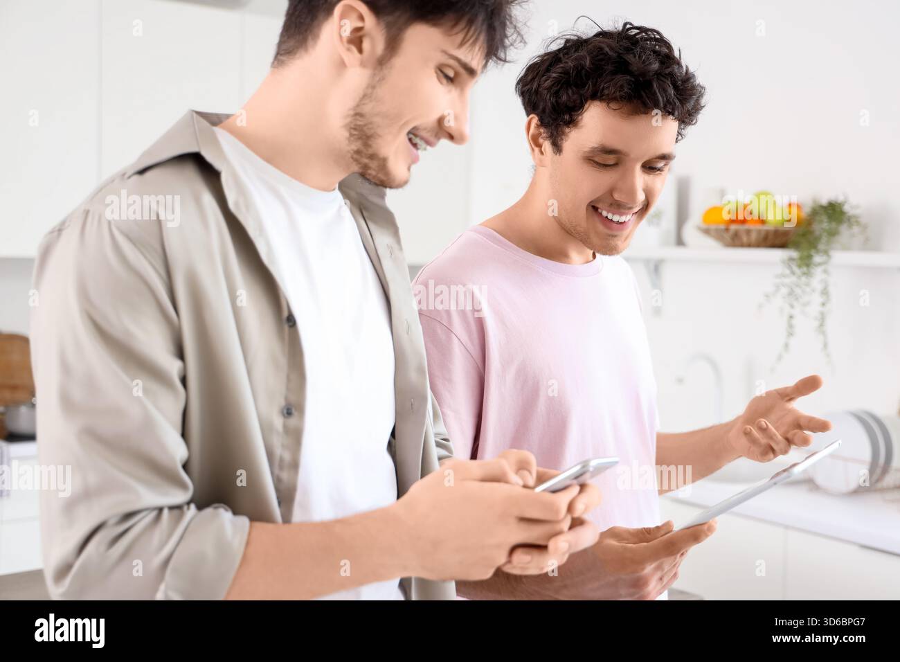 Young brothers using tablet computer and mobile phone in kitchen Stock Photo
