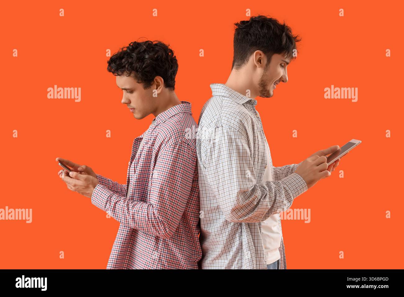 Young brothers using tablet computer and mobile phone on orange background Stock Photo