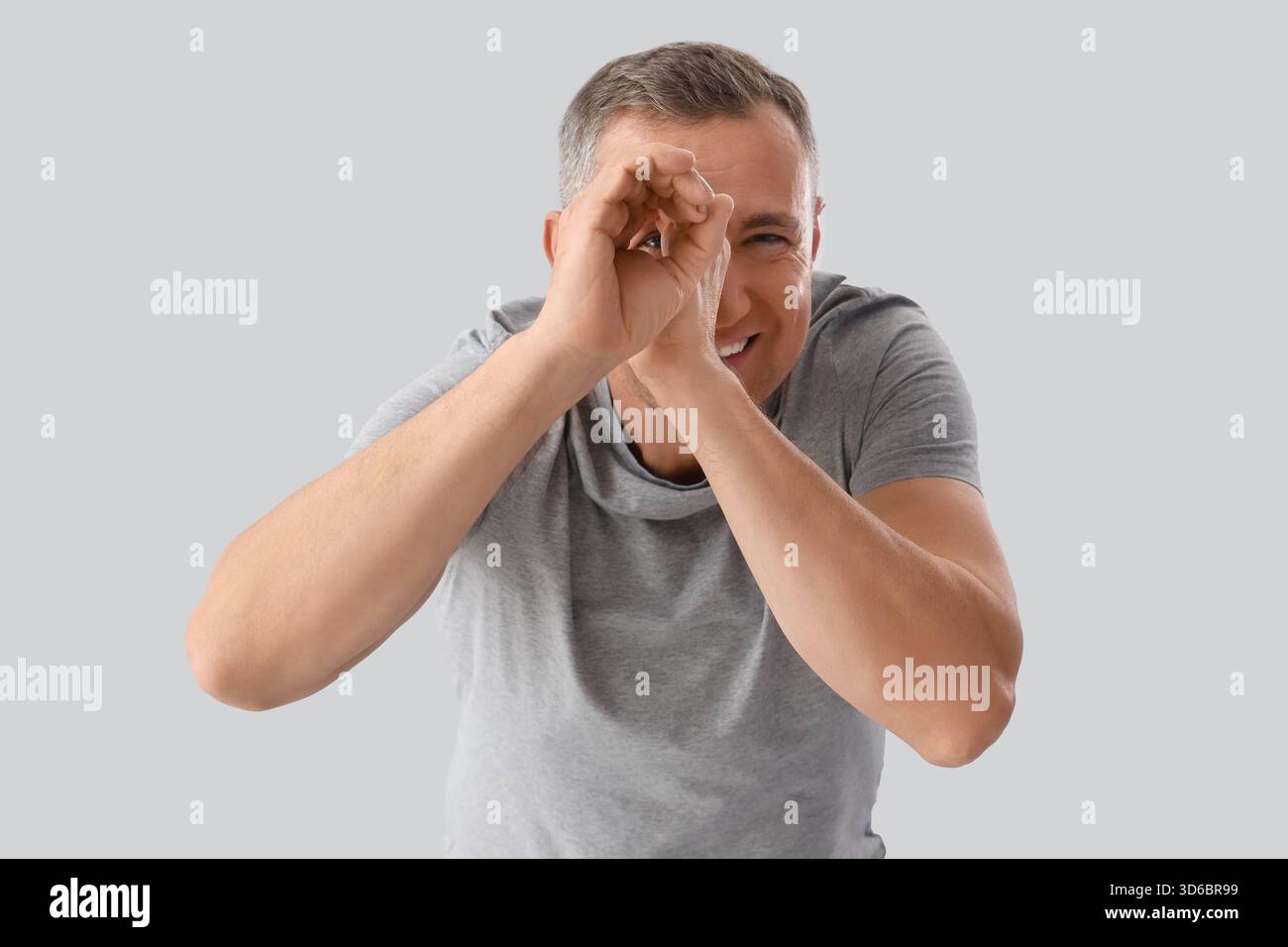 Mature man looking through imaginary telescope on light background Stock Photo