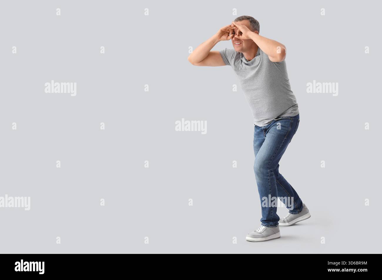 Mature man looking through imaginary binoculars on light background Stock Photo