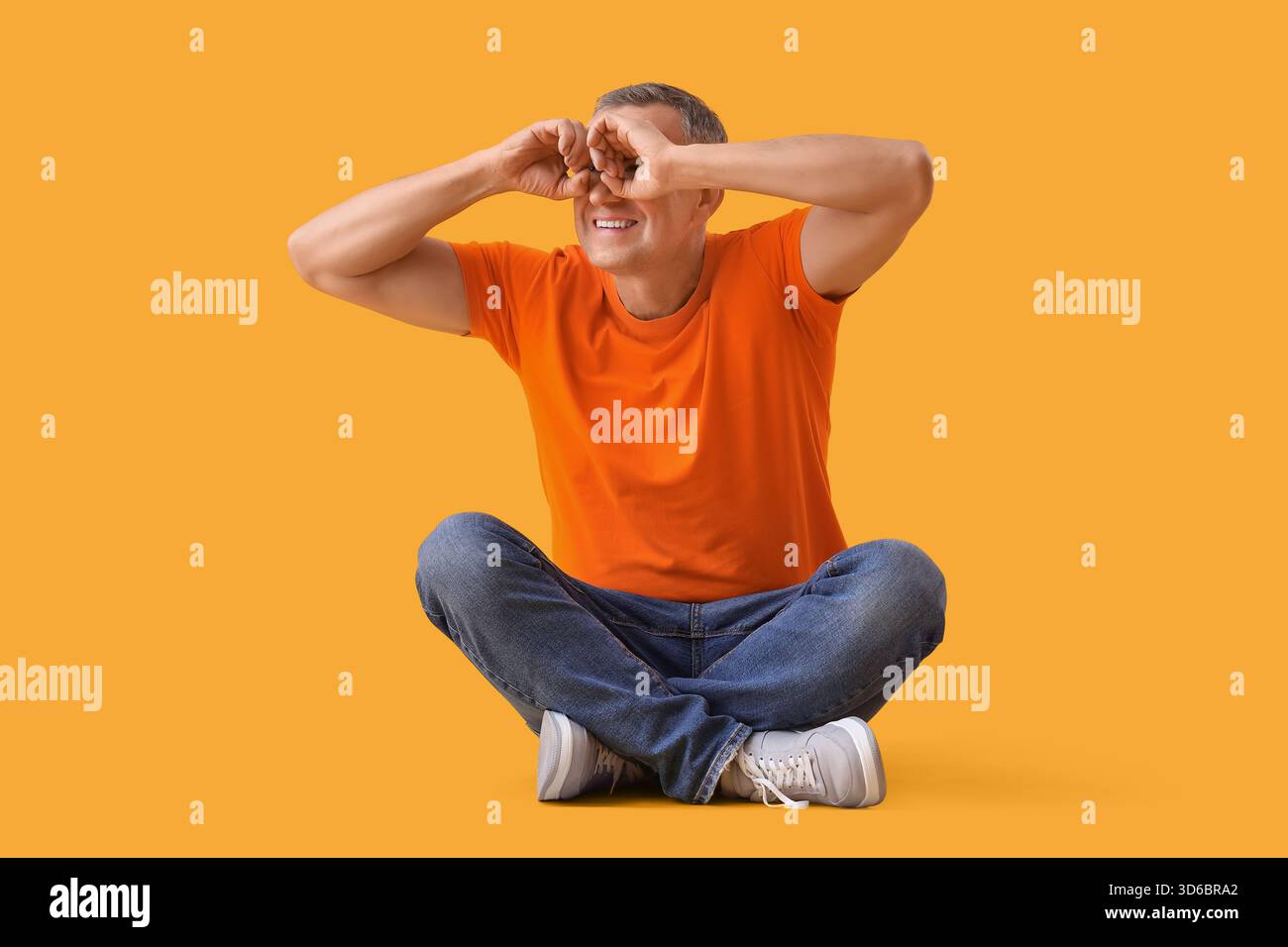 Mature man looking through imaginary binoculars on yellow background Stock Photo