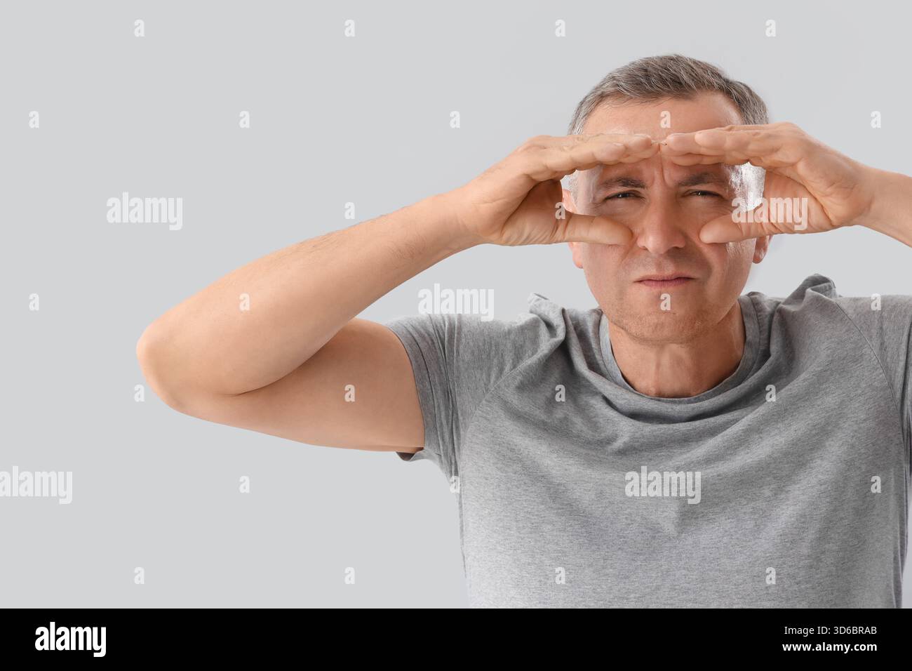 Mature man looking through imaginary binoculars on light background Stock Photo