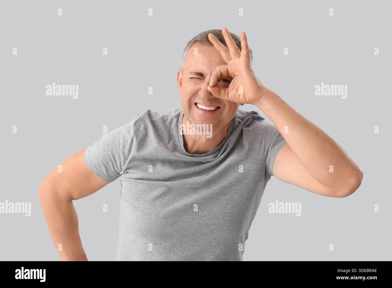 Mature man looking through imaginary telescope on light background Stock Photo