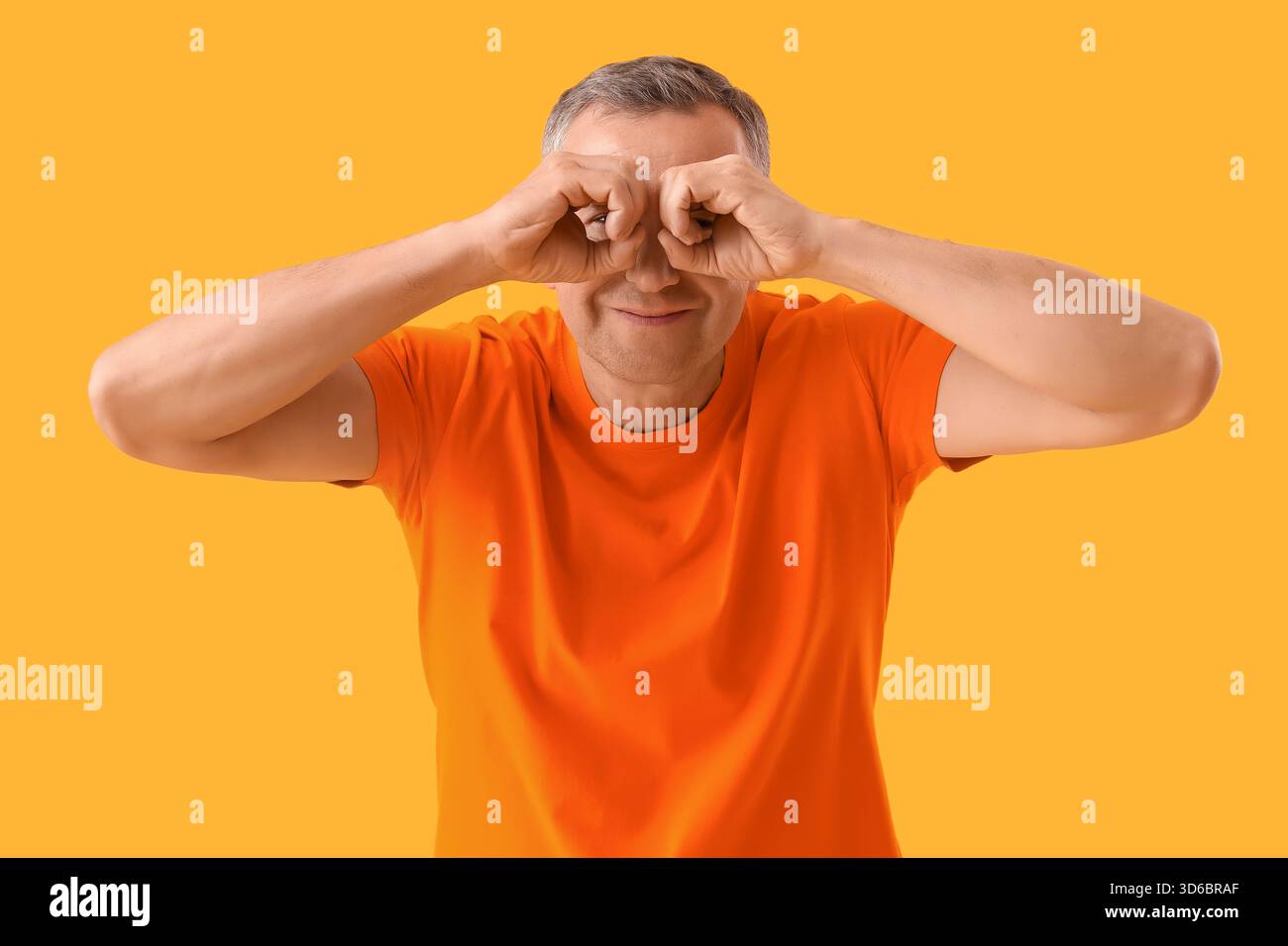 Mature man looking through imaginary binoculars on yellow background Stock Photo