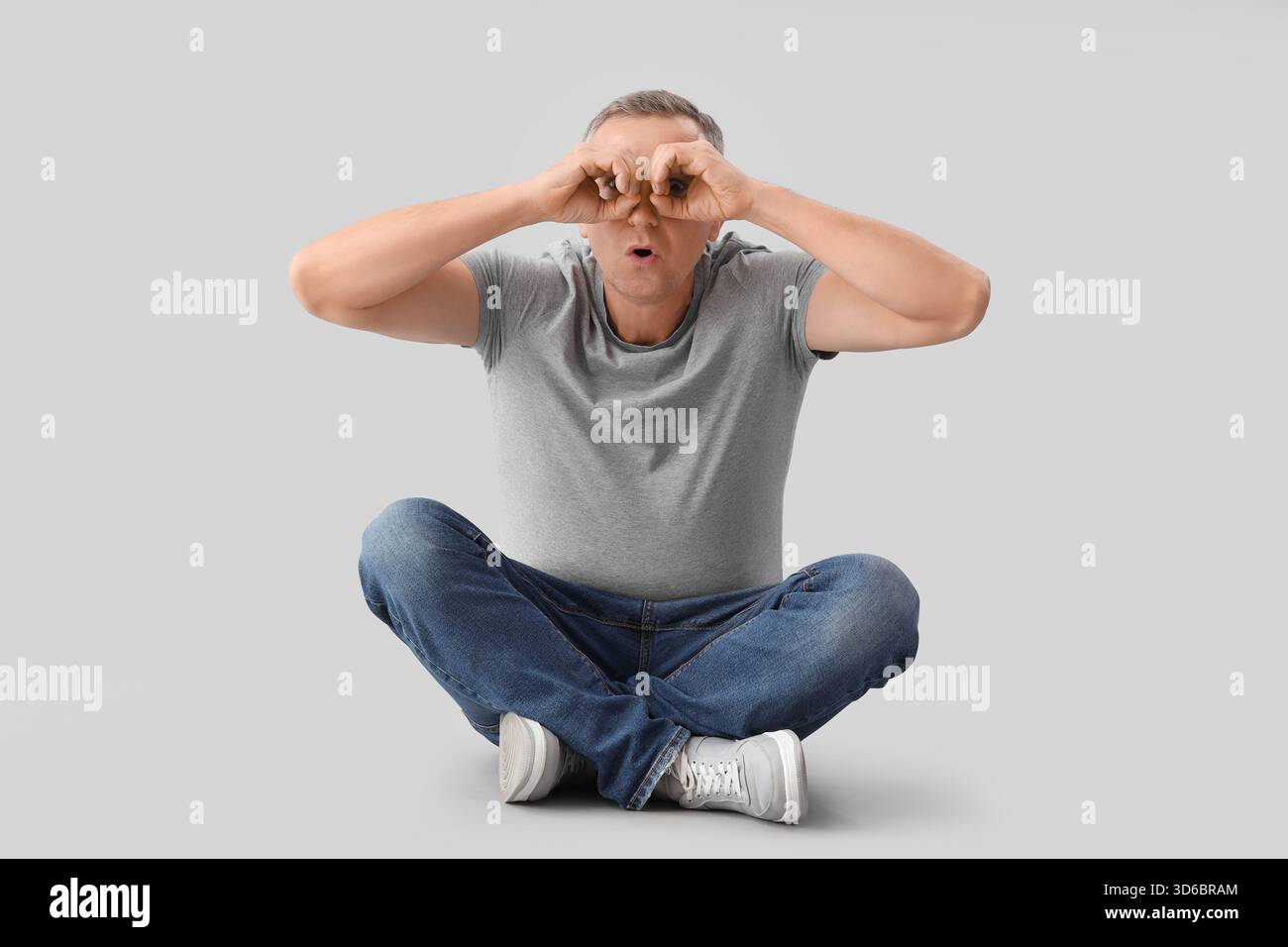 Mature man looking through imaginary binoculars on light background Stock Photo