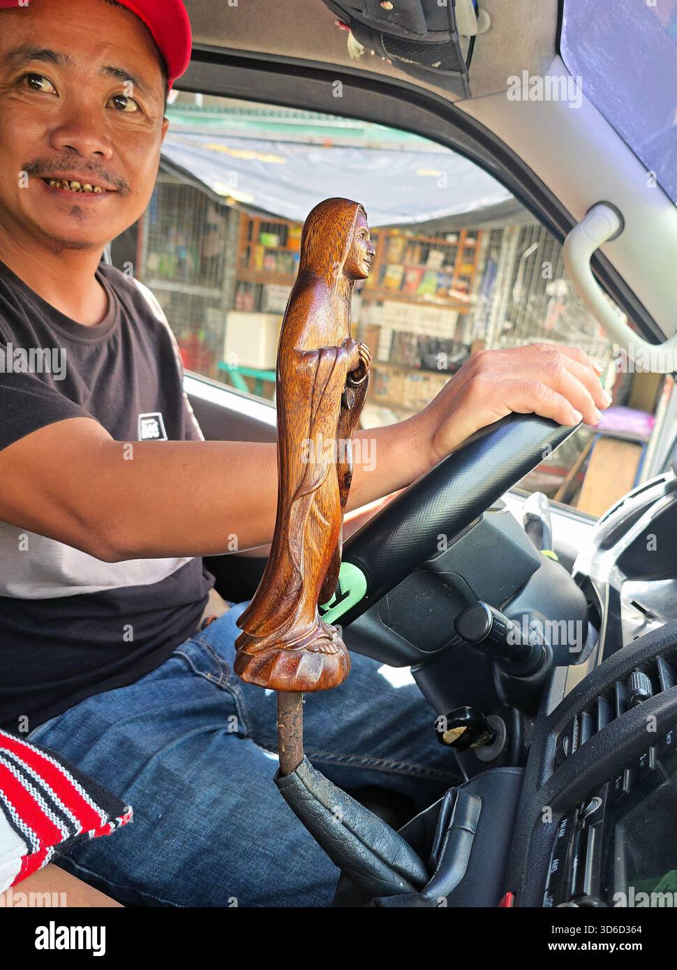 A Happy Driver In Car With a Mother Mary Wooden Statue Gear Shift Ornament Inside Vehicle - Smartphone Captured Stock Image