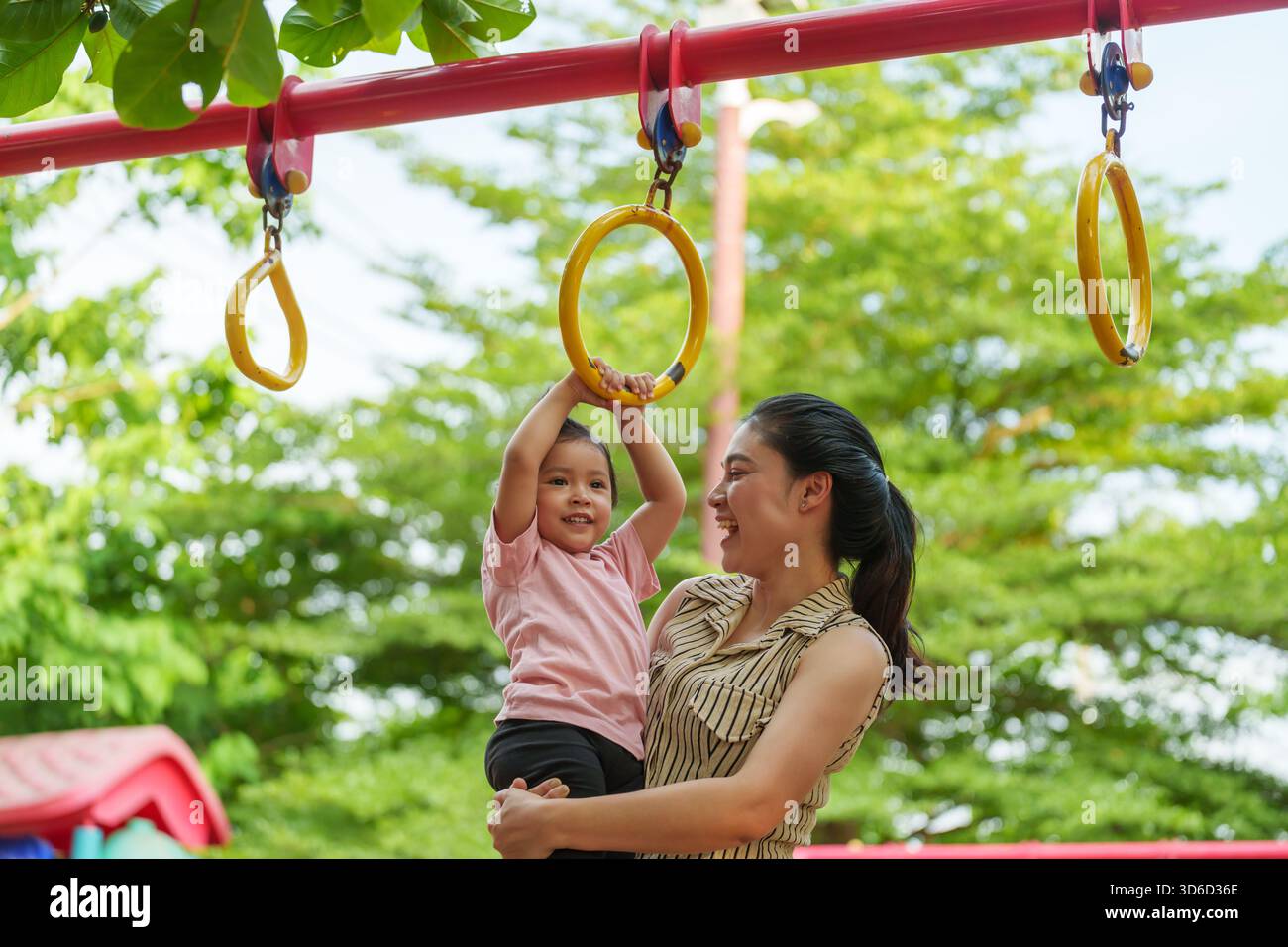 Kids Using Playground Rings mother holding her daughter to hanging on playground rings in the park ...
