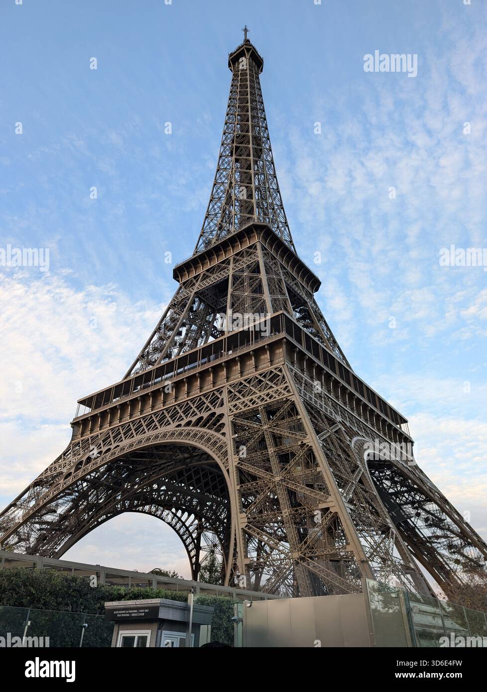 The Eiffel Tower in Paris, France, photographed from a low angle with its iron lattice structure rising into a blue, lightly clouded sky. A clear dayt - Smartphone Captured Stock Image