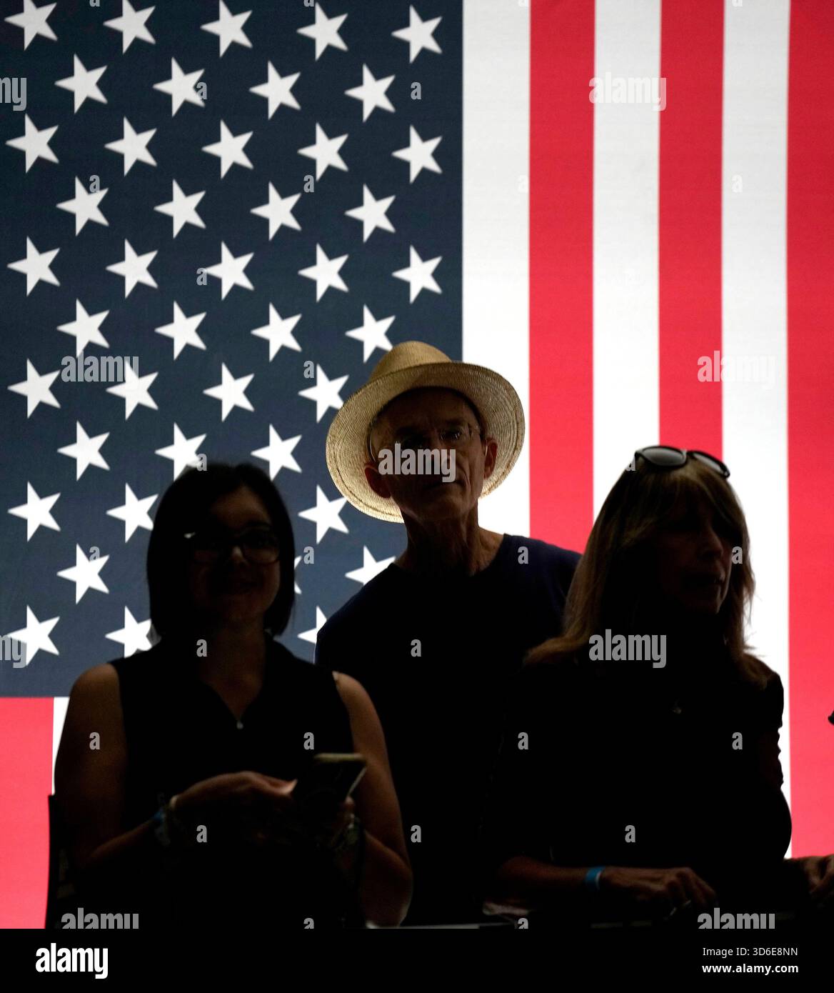 Attendees are silhouetted in front of an American flag as they waited ...