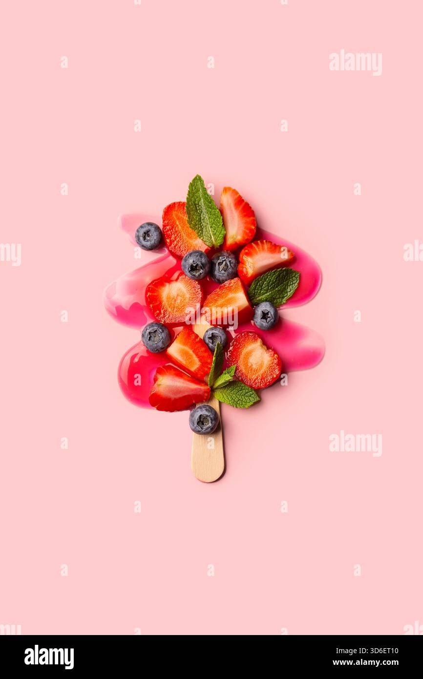 A vibrant image showcasing a fruit popsicle mid-melt with strawberries and blueberries on a soft pink background. Stock Photo