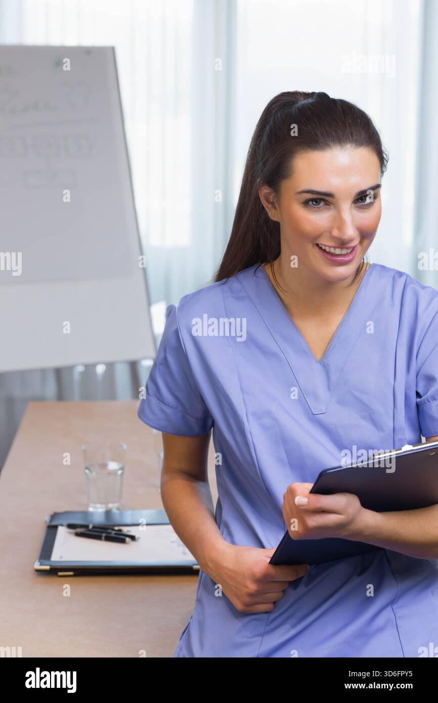 Female nurse in purple scrubs holding dark clipboard and leaning at ...