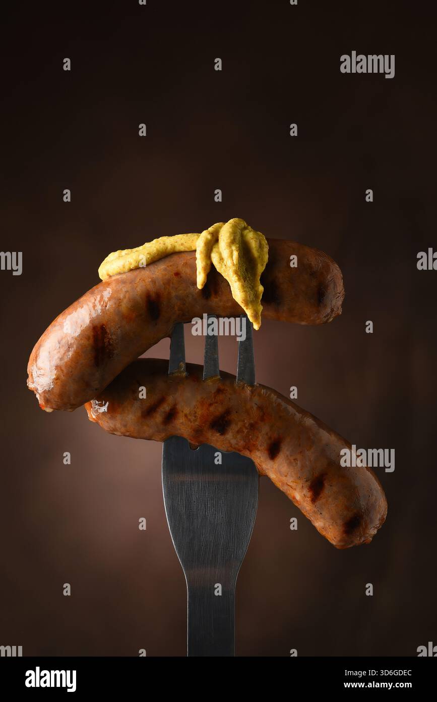 Two grilled sausages on fork with mustard Stock Photo