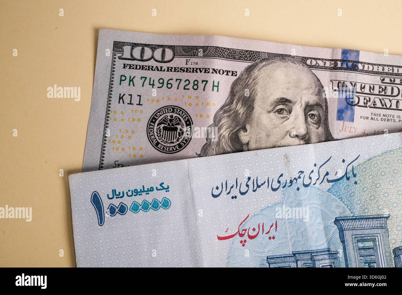 A close-up of a 100 dollar bill and an Iranian rial banknote on a light ...