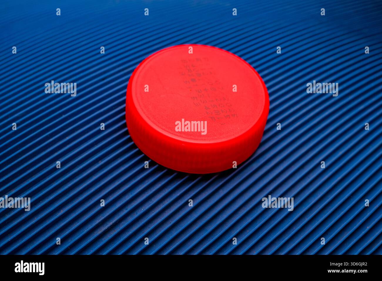 Vibrant Red Round Plastic Cap on Deeply Textured Diagonal Blue Ribbed Surface Stock Photo