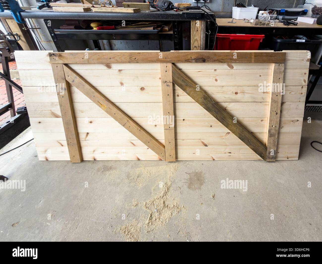 Newly built wooden shed door or garden gate with diagonal supports lying on concrete floor in workshop surrounded by tools and workbench - Smartphone Captured Stock Image