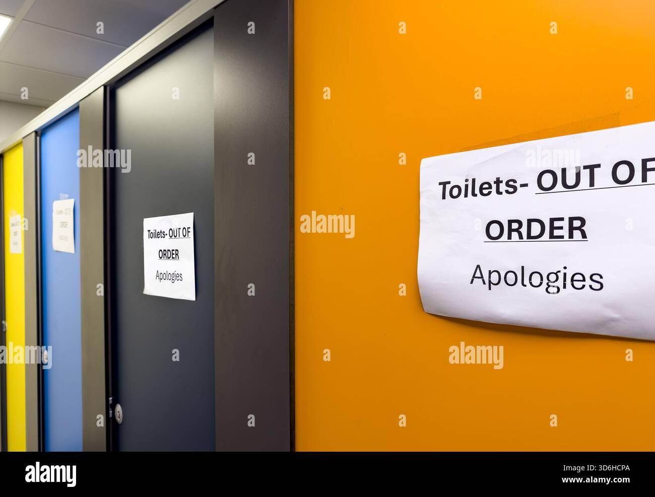 Out of order signs on multi coloured bathroom toilet stall doors in a public or commercial building hallway - Smartphone Captured Stock Image