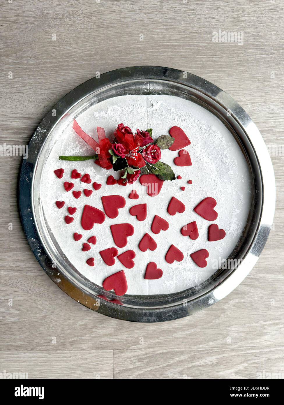 Round metal tray with powdered sugar & decorated with red heart icing sugar cutouts sugarcraft & small artificial flower arrangement valentines day - Smartphone Captured Stock Image
