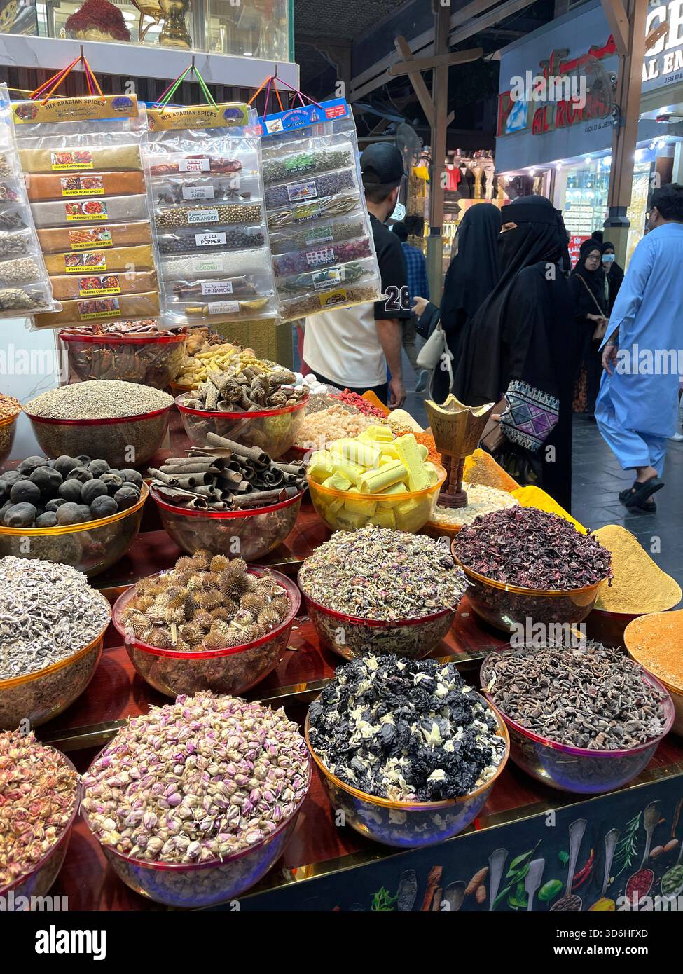 Colourful display of dried herbs, spices, and flowers in metal bowls at busy traditional spice market souk & people walking in background Dubai UAE - Smartphone Captured Stock Image