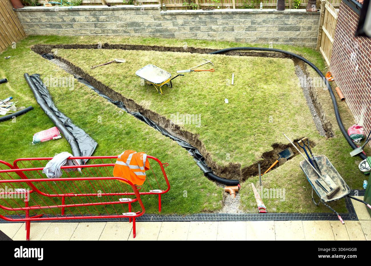 Residential backyard undergoing groundwork and drainage installation of a field drain with tools scattered and trenching in progress - Smartphone Captured Stock Image