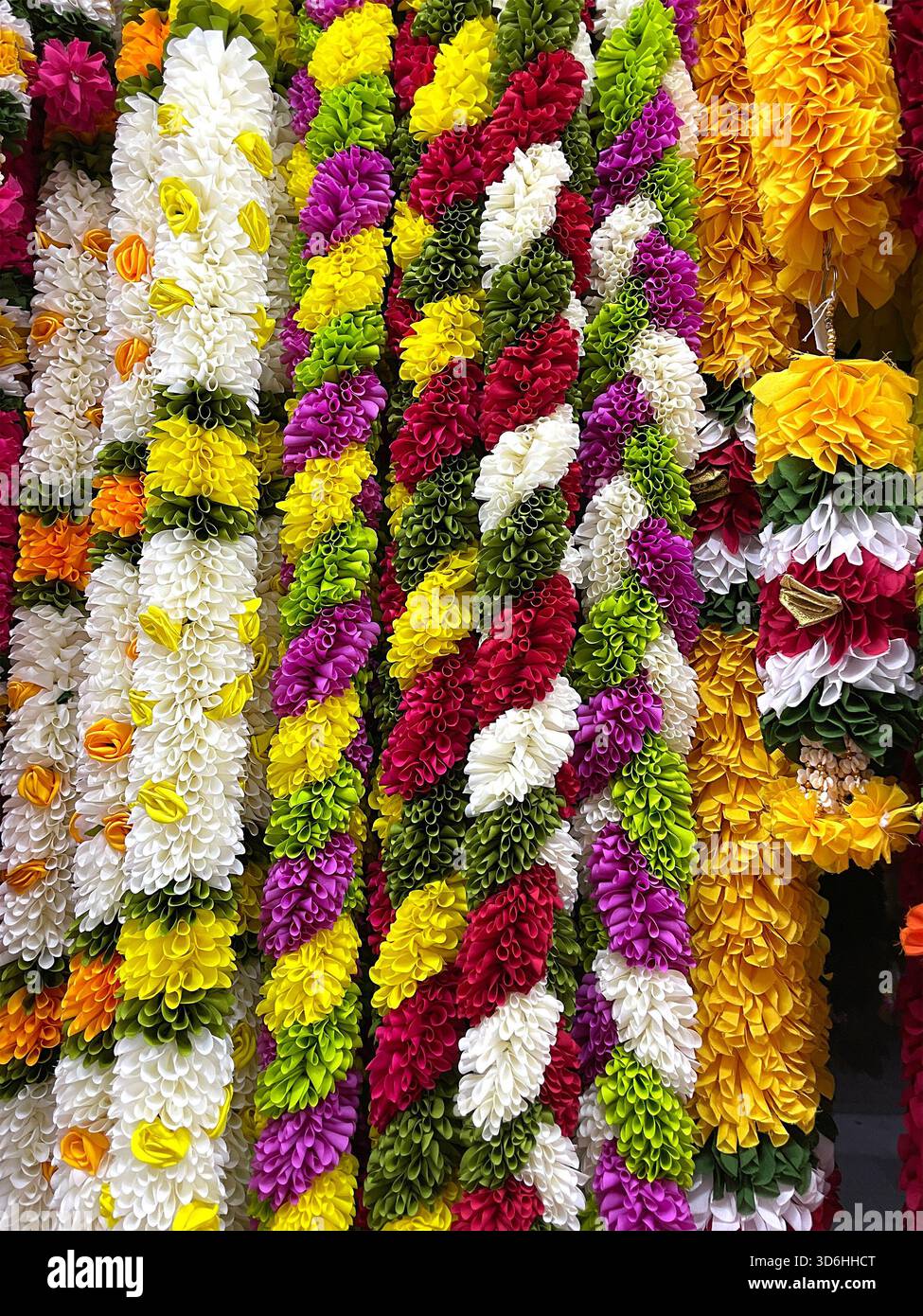 Multi Coloured artificial flower garlands arranged vertically in a market display for indian asian cultural festivals or traditional ceremonies Stock Photo