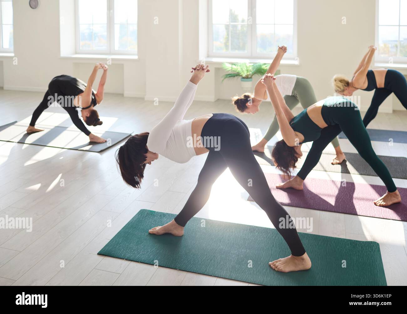 Group yoga class practicing wide-legged forward bends in bright sunny studio Stock Photo