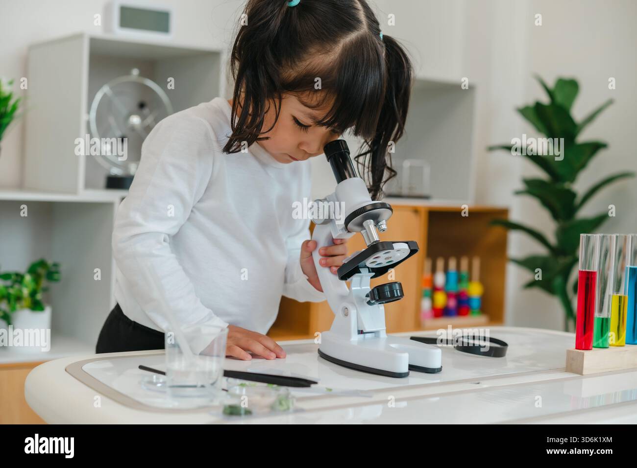 toddler girl scientist looking through a microscope. learning science Stock Photo