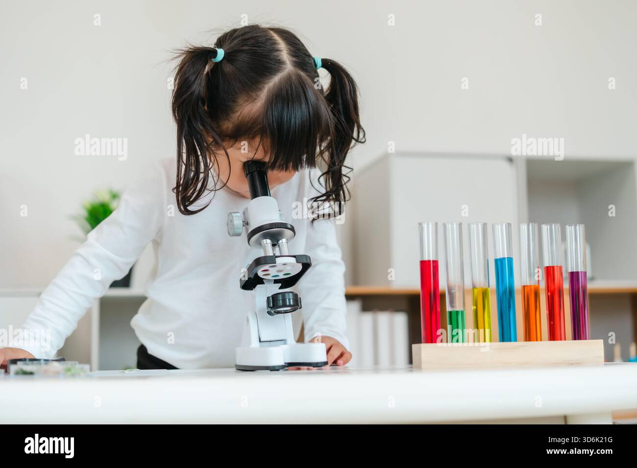 toddler girl scientist looking through a microscope. learning science Stock Photo