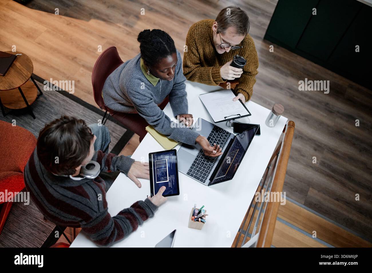 Diverse Young Adults Collaborating on Project Using Laptop in Modern Office Stock Photo