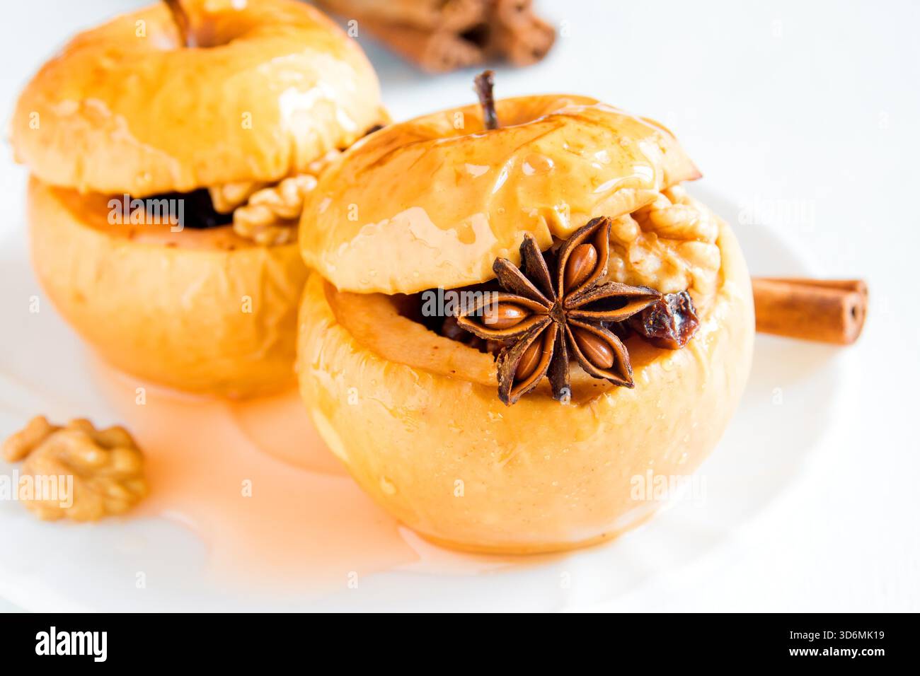 baked apples stuffed with dried fruit, nuts, cinnamon, anise and honey on white plate close up Stock Photo