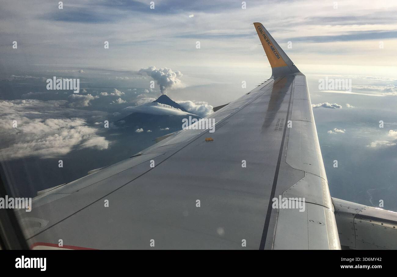 Legazpi, Philippines, Southeast Asia: Aerial view from Cebu Pacific airplane window of Mayon volcano erupting, volcanic ash plume rising above summit - Smartphone Captured Stock Image