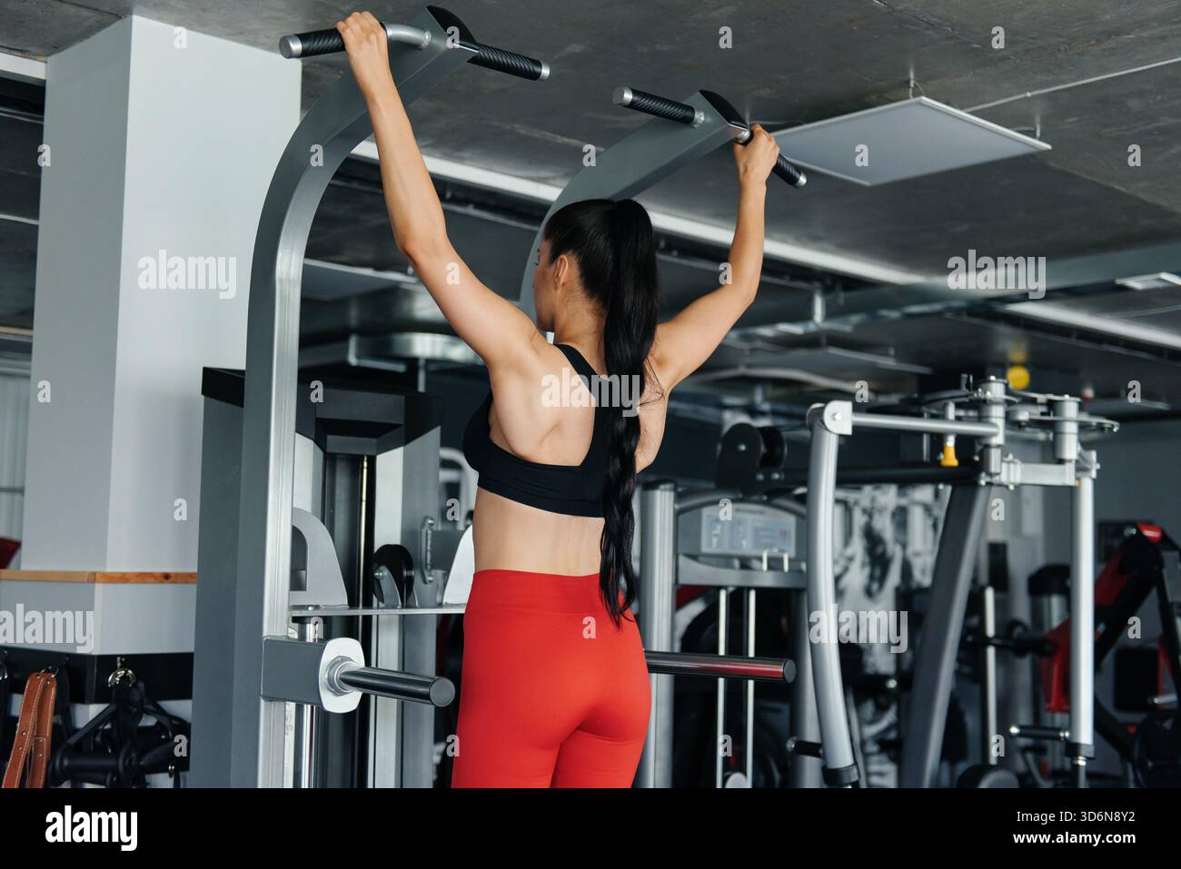 Muscular young woman doing pull up exercises on simulator Stock Photo