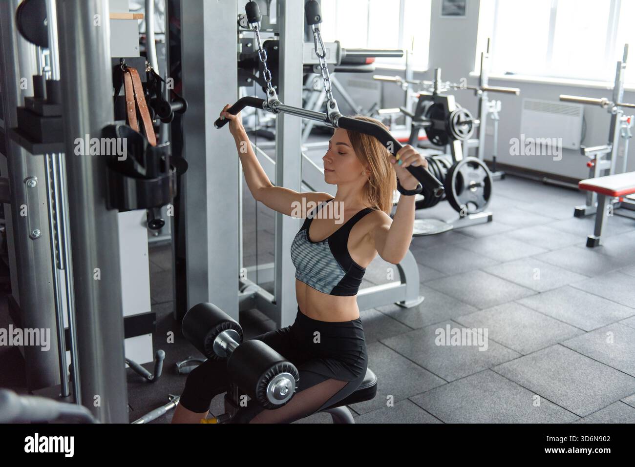 Muscular young woman doing pull up exercises on simulator Stock Photo