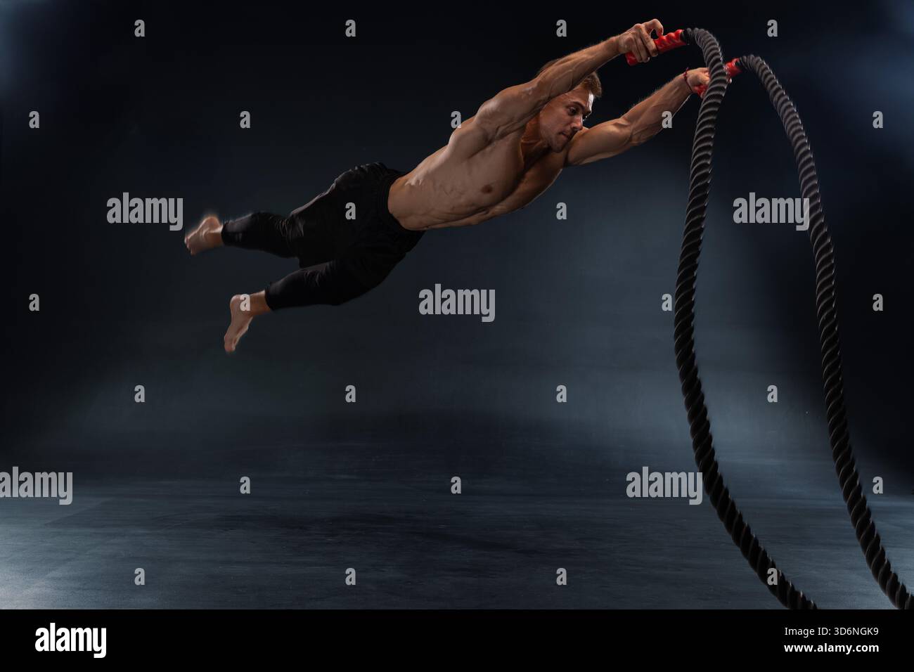 Drooping Rope Middle muscular man is leaping off the ground while gripping heavy battle ...