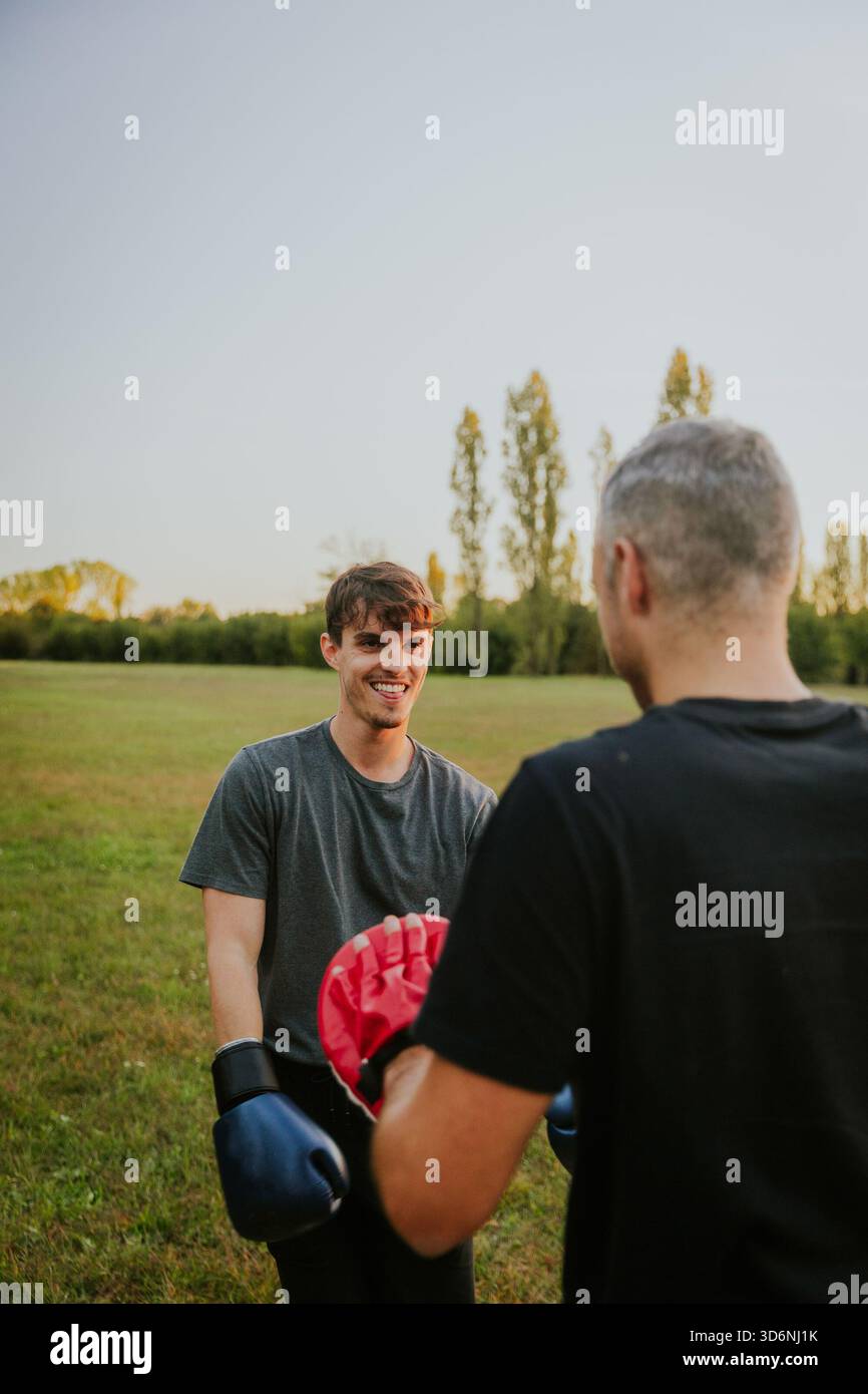 Two men training with boxing gloves in autumn park at sunset. Stock Photo