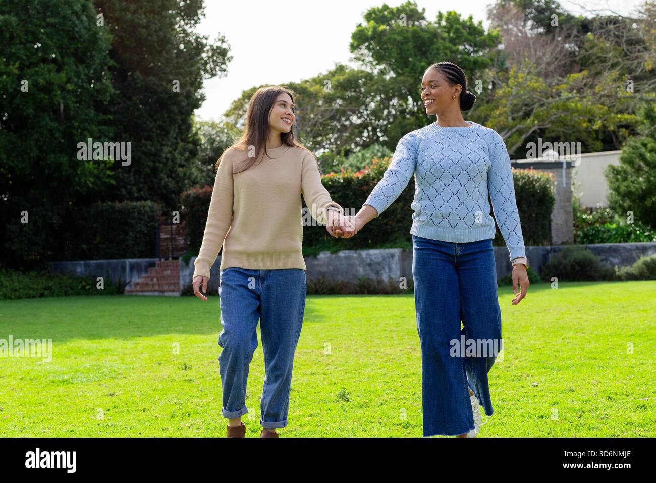 Diverse women walking hand in hand across garden lawn beside stone wall ...