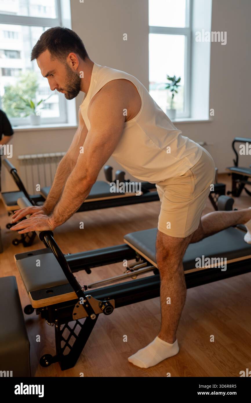 Image result for Pilates trainer provides guided support for male client during reformer ...