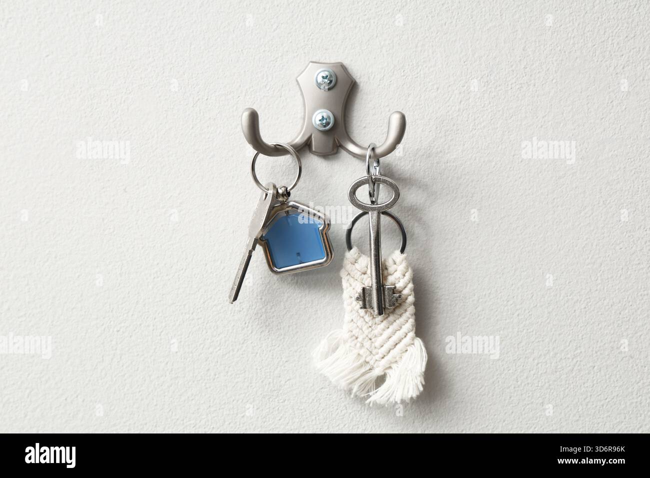 Keys from house hanging on hooks on light wall Stock Photo